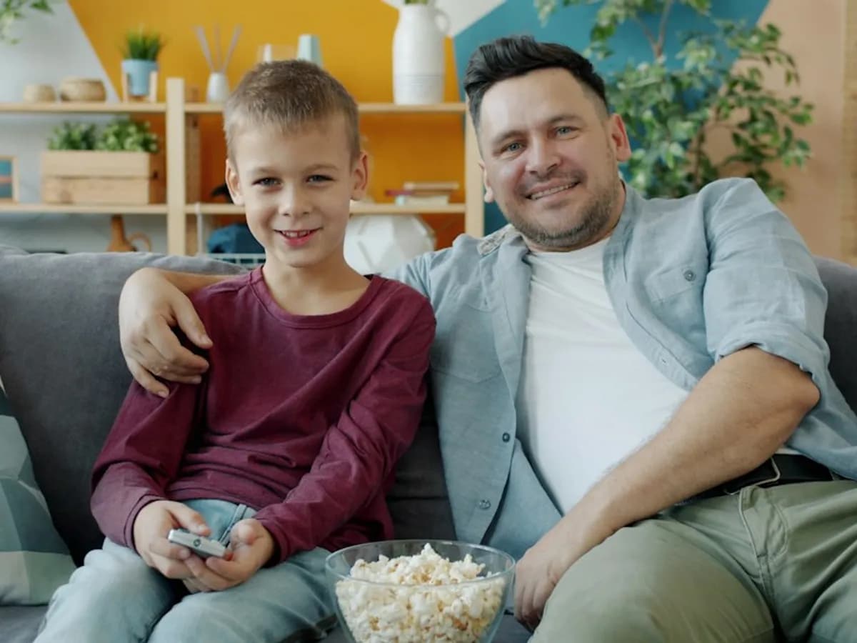 A father and son on the sofa with popcorn and a remote, about to watch TV together