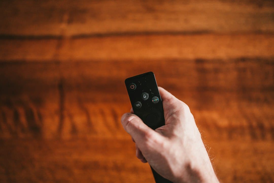 A person on a sofa with a TV remote, comparing IPTV services before choosing Varesteam4K